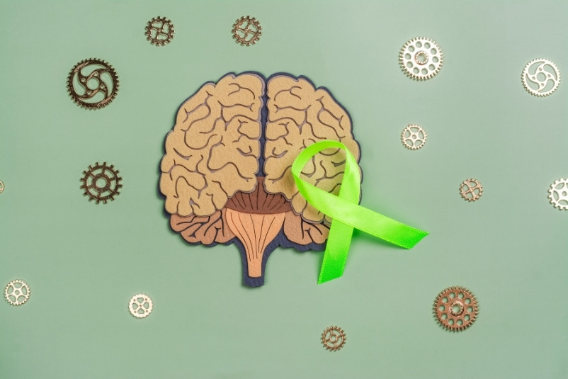 Brain surrounded by gears underneath a green ribbon for mental health awareness.